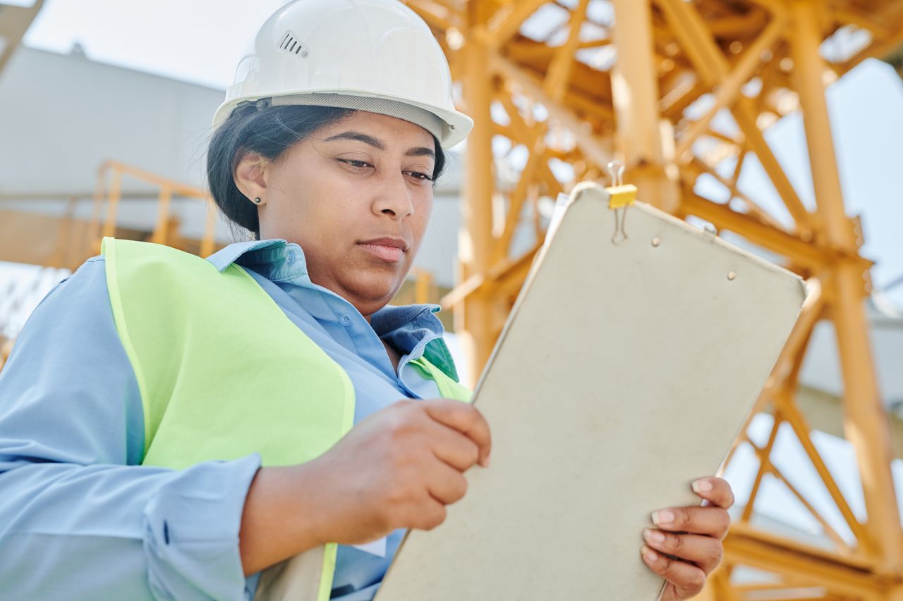 our-experience Confident female construction worker inspecting site with clipboard and helmet.